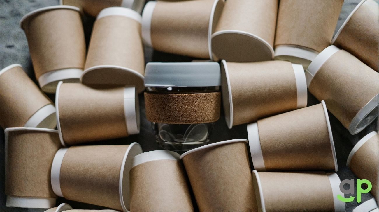 Pile of discarded paper cups with a single glass bottle in the center, highlighting the contrast between disposable and reusable packaging.